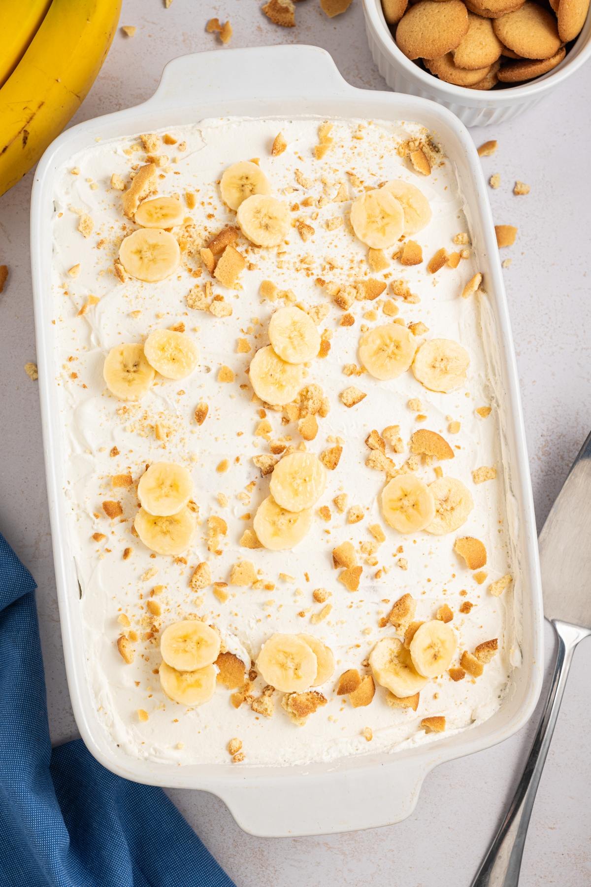 Banana pudding topped with banana slices and crushed vanilla wafers in a white dish.