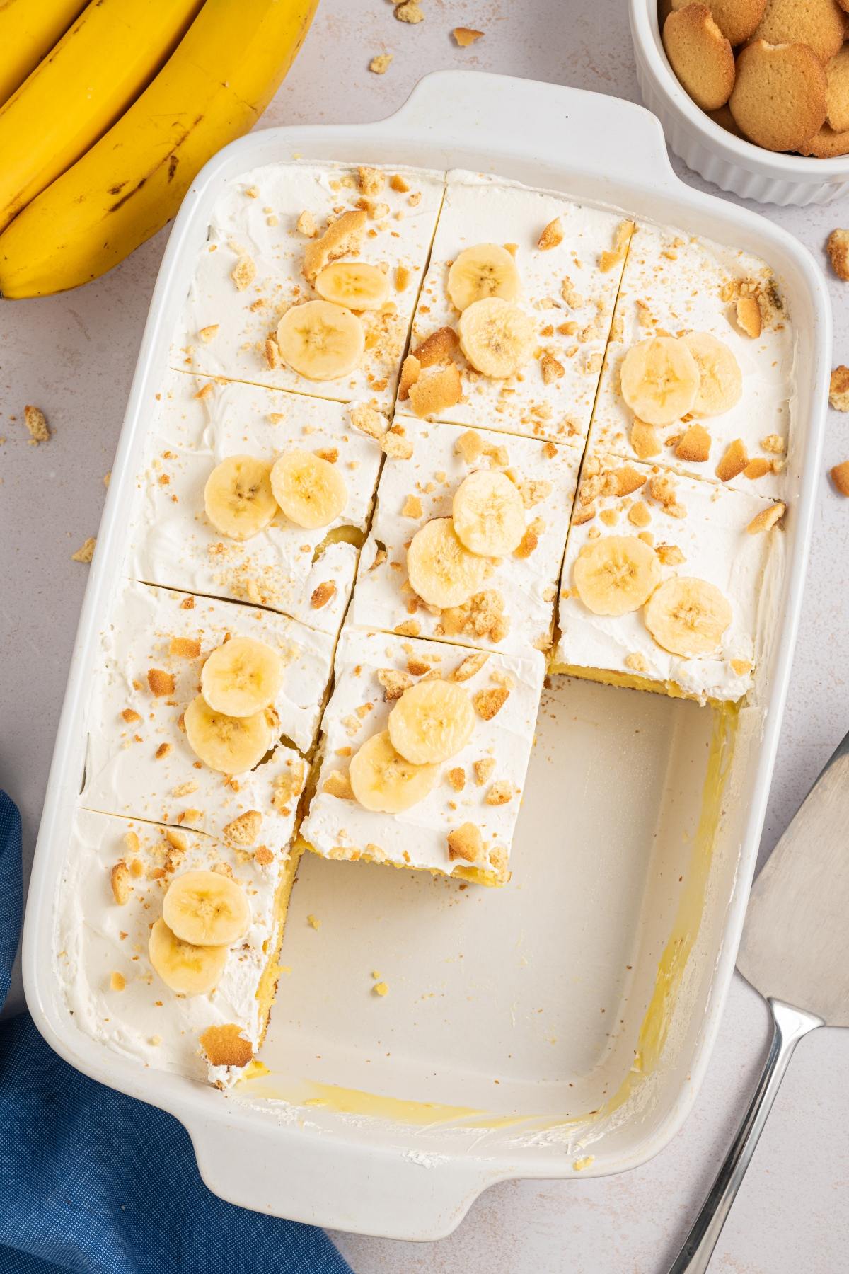 Slices of banana pudding topped with banana slices and crumbled cookies in a white baking dish.