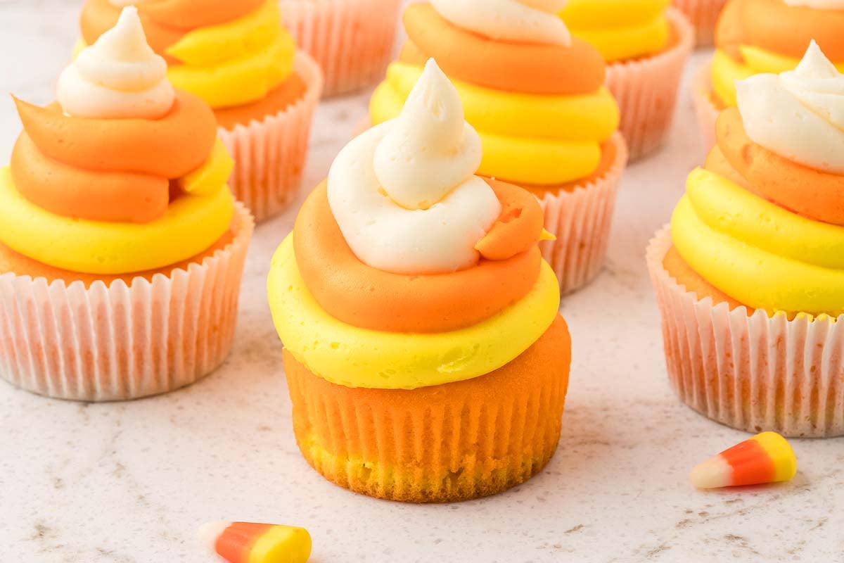 Candy corn cupcakes topped with orange, yellow, and white swirled frosting, resembling classic Halloween treats, on a white surface.