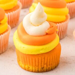 Candy corn cupcakes with orange, yellow, and white swirled frosting are styled to look just like the classic Halloween treat.