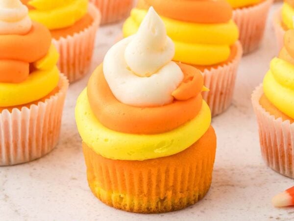 Candy corn cupcakes with orange, yellow, and white swirled frosting are styled to look just like the classic Halloween treat.