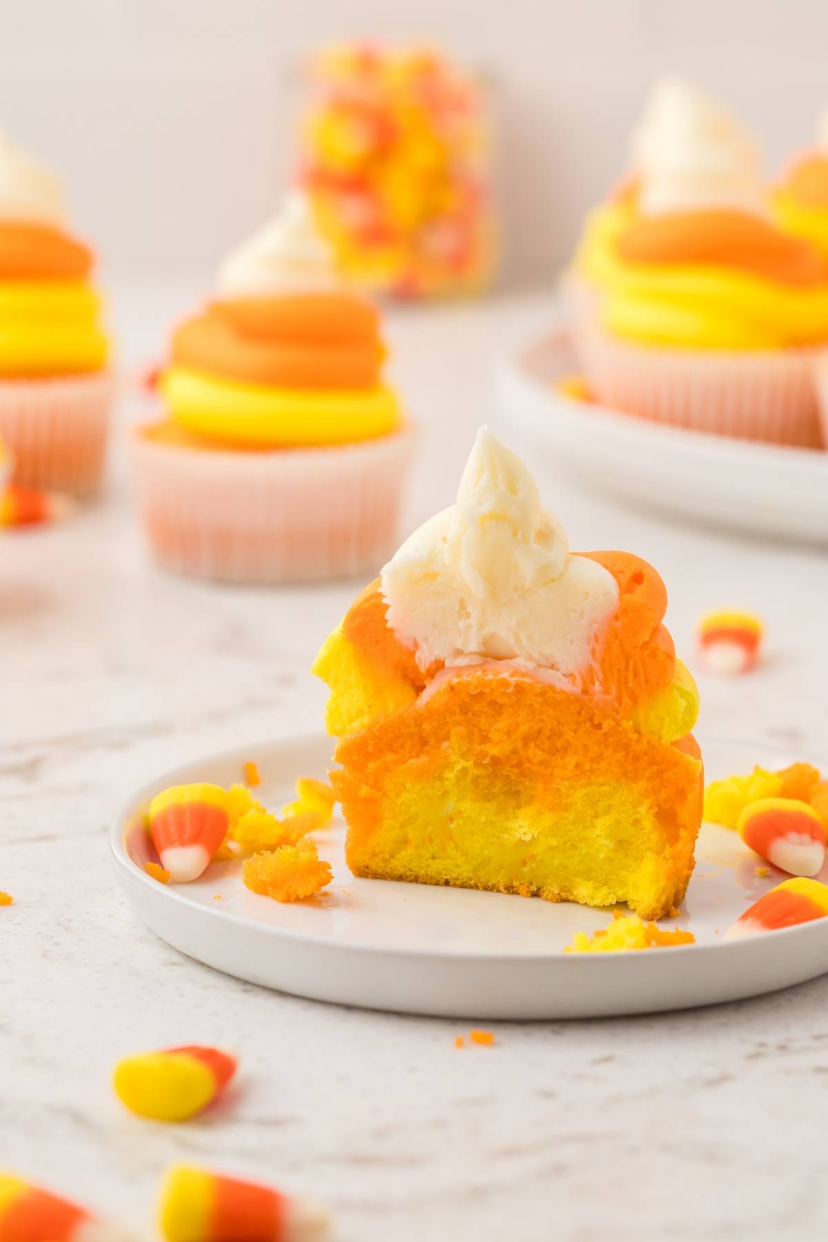 A cupcake with yellow and orange layers, white frosting, and candy corn, sliced in half on a plate.