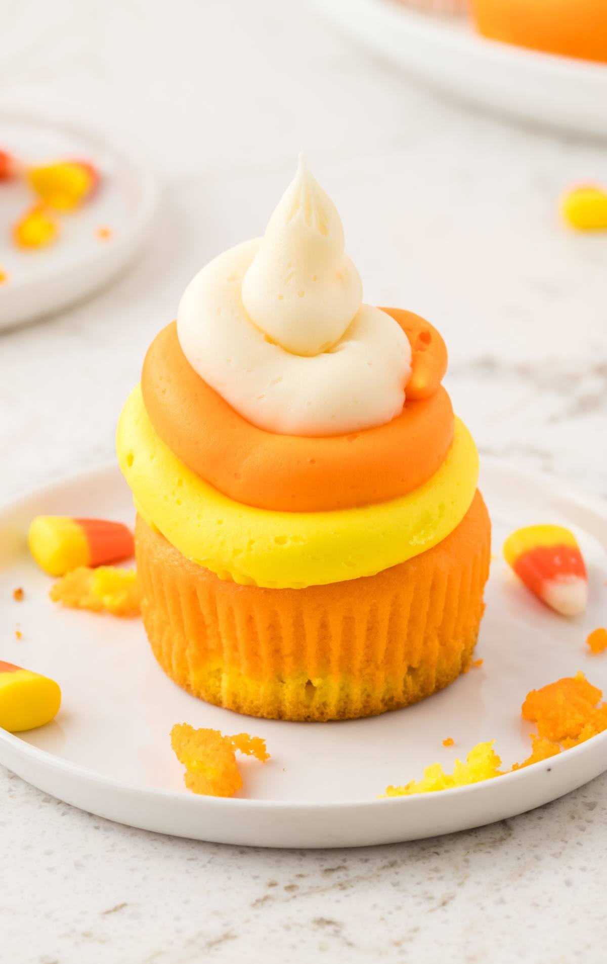 Cupcake with yellow, orange, and white swirled frosting, decorated with candy corn, on a white plate.