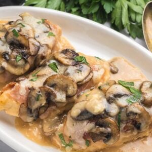 Three pieces of chicken Valdostana topped with mushrooms and melted cheese on a white plate with creamy sauce.