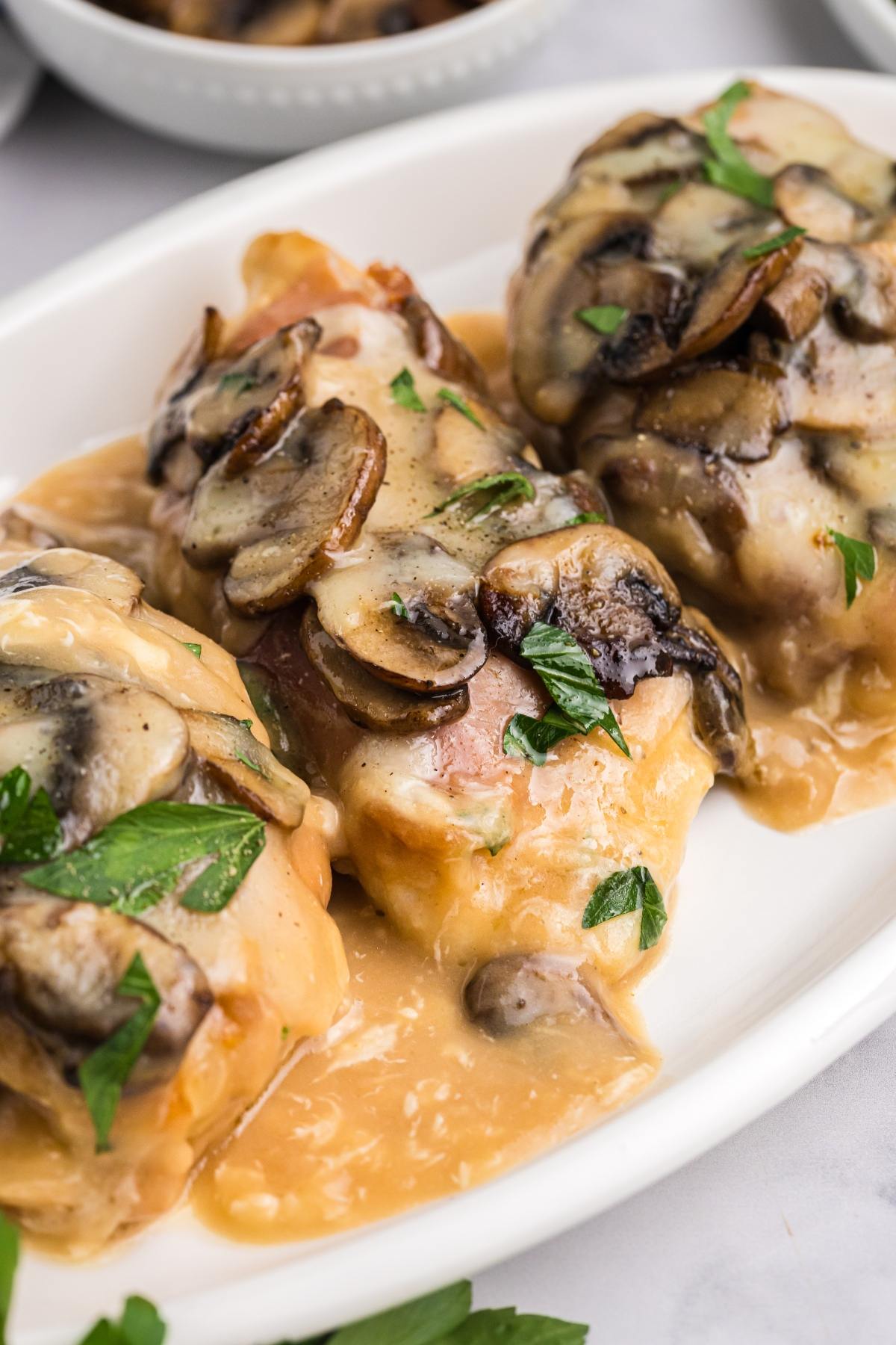 Chicken breasts topped with sautéed mushrooms and melted cheese, garnished with parsley on a white plate.