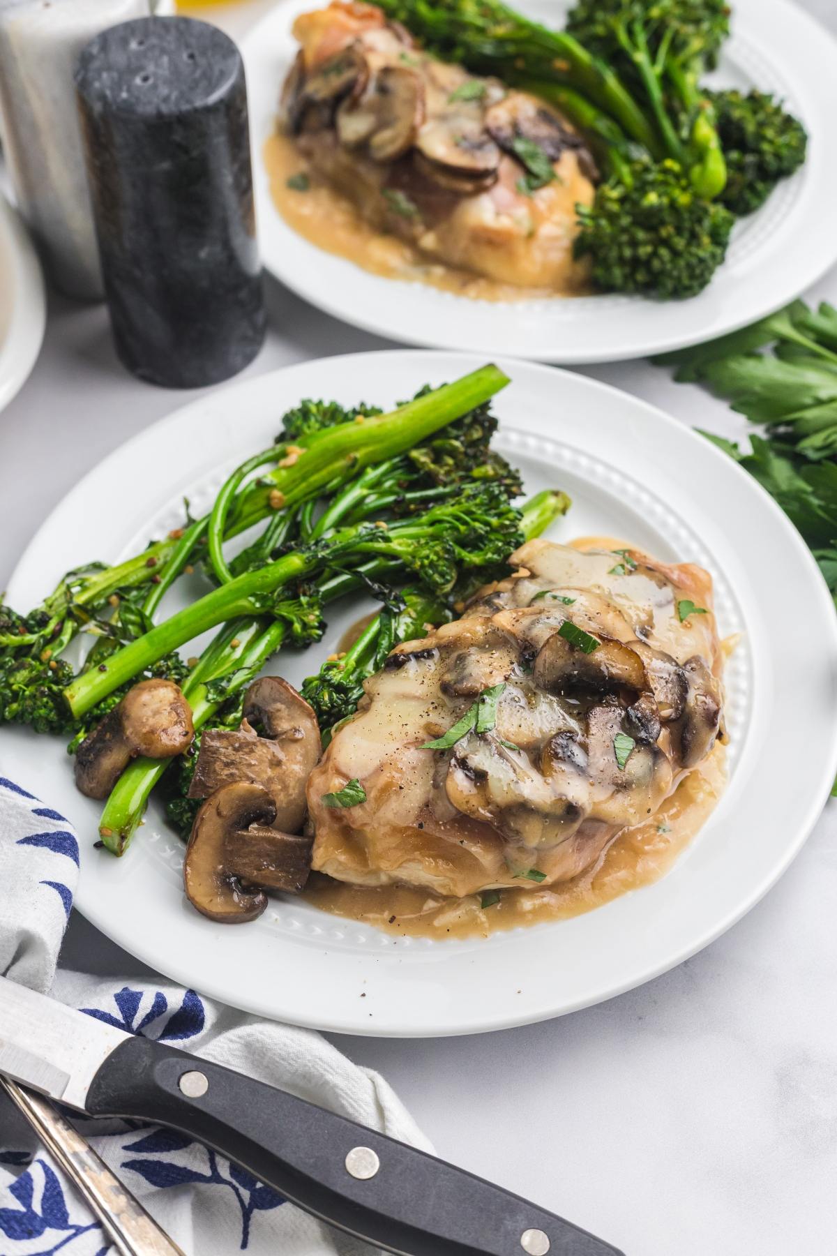 Chicken breast with mushroom sauce and steamed broccolini served on a white plate, garnished with herbs.
