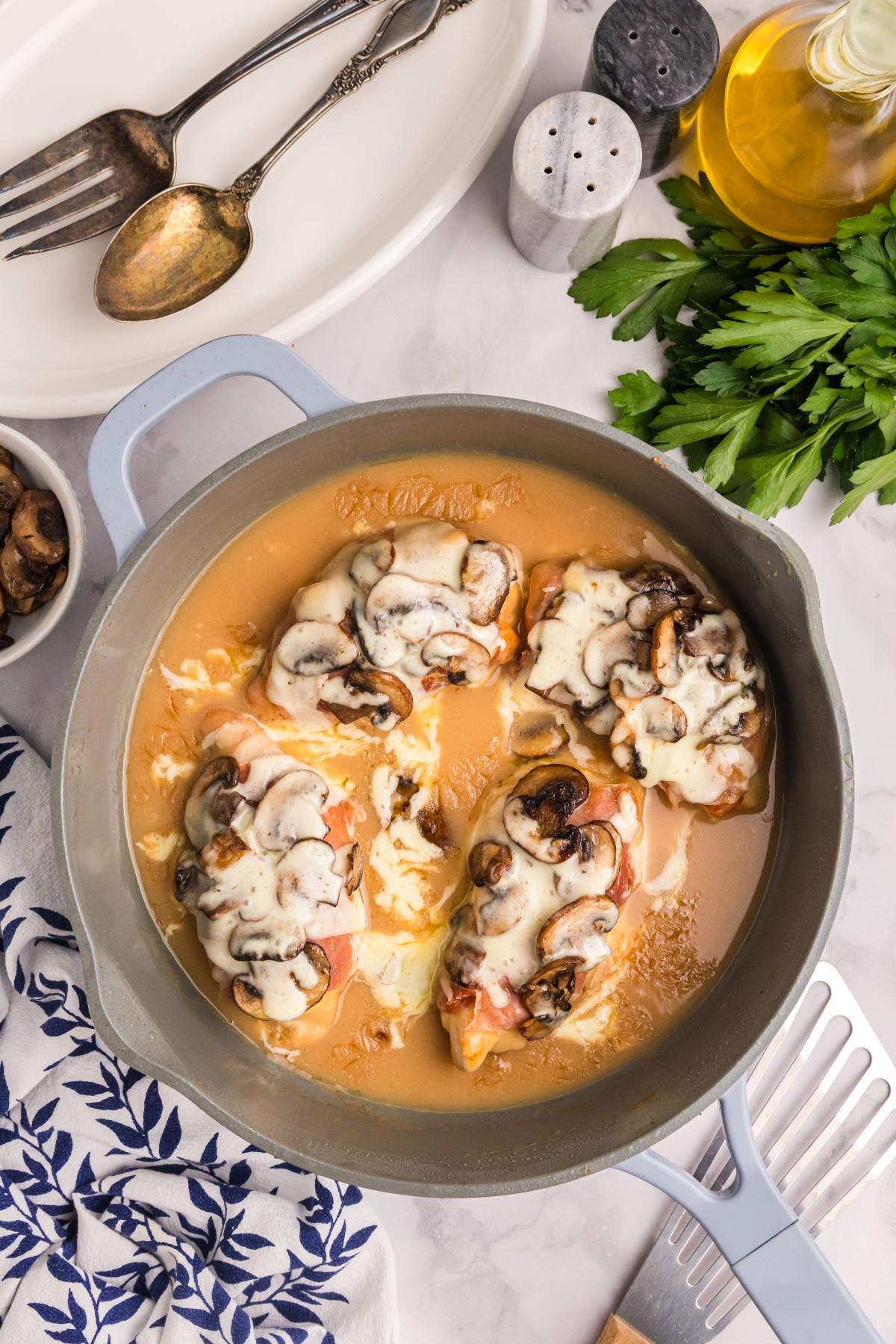 Chicken breasts topped with mushrooms and melted cheese in a creamy sauce in a blue skillet.