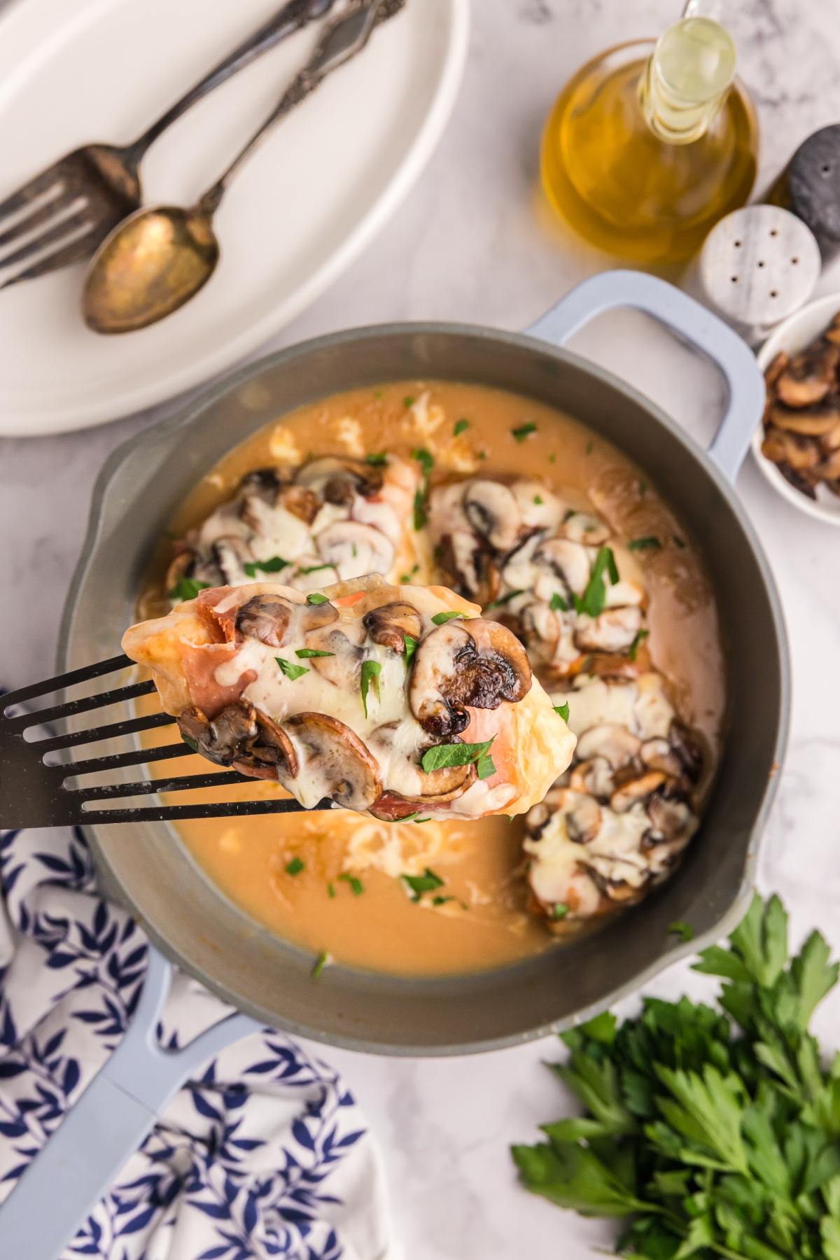 A spatula lifts cheesy, mushroom-topped chicken from a skillet with creamy sauce.