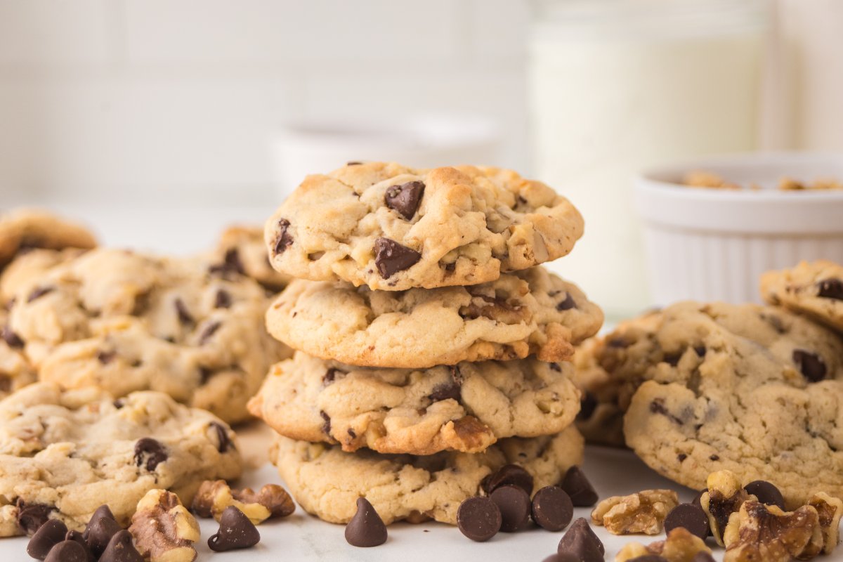A stack of chocolate chip walnut cookies surrounded by more cookies, chocolate chips, and walnuts.