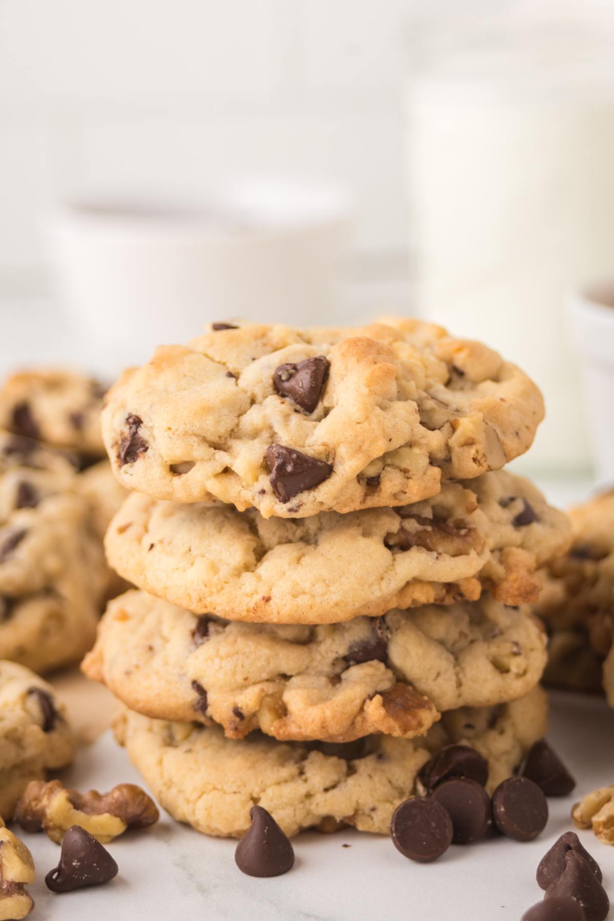 A stack of chocolate chip cookies with scattered chocolate chips on a white surface.
