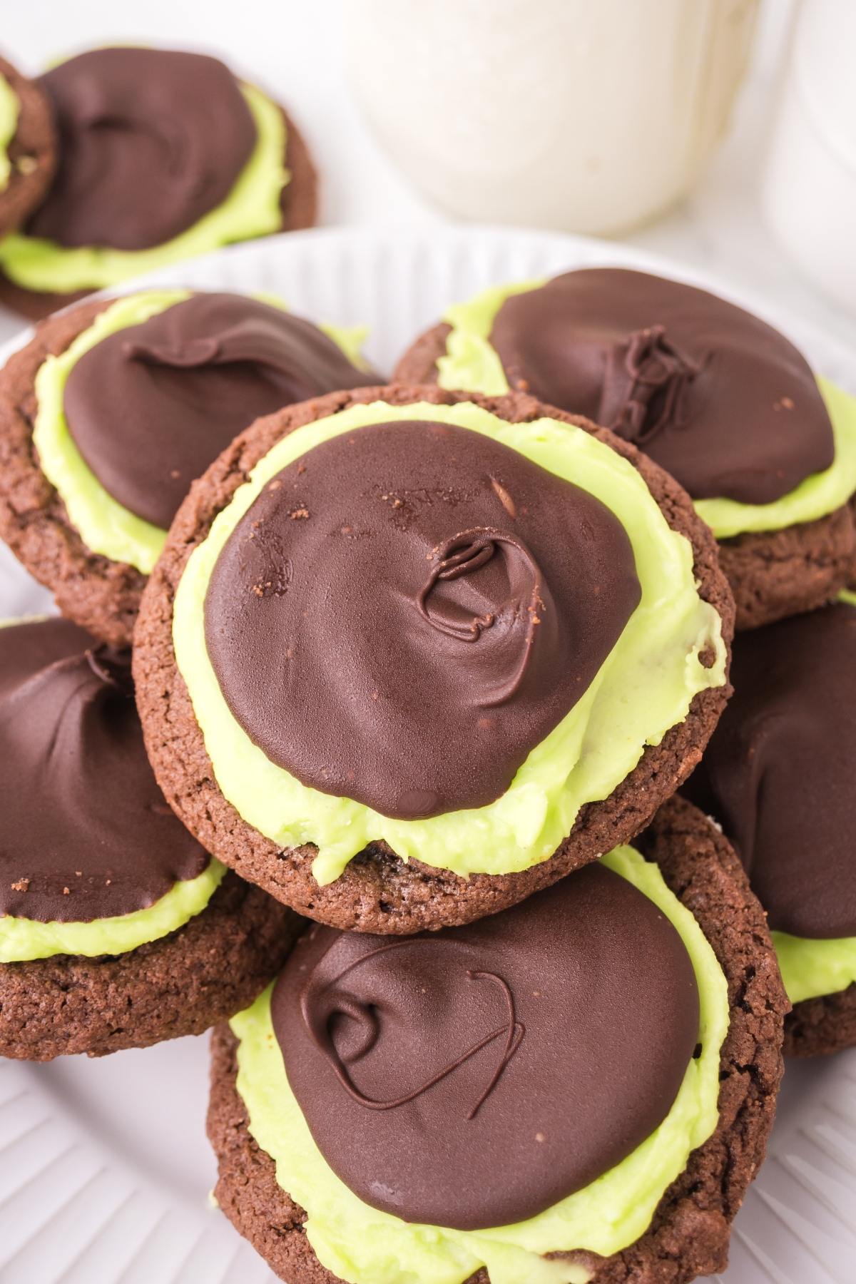 Chocolate cookies with green mint frosting and a layer of chocolate on top, stacked on a white plate.