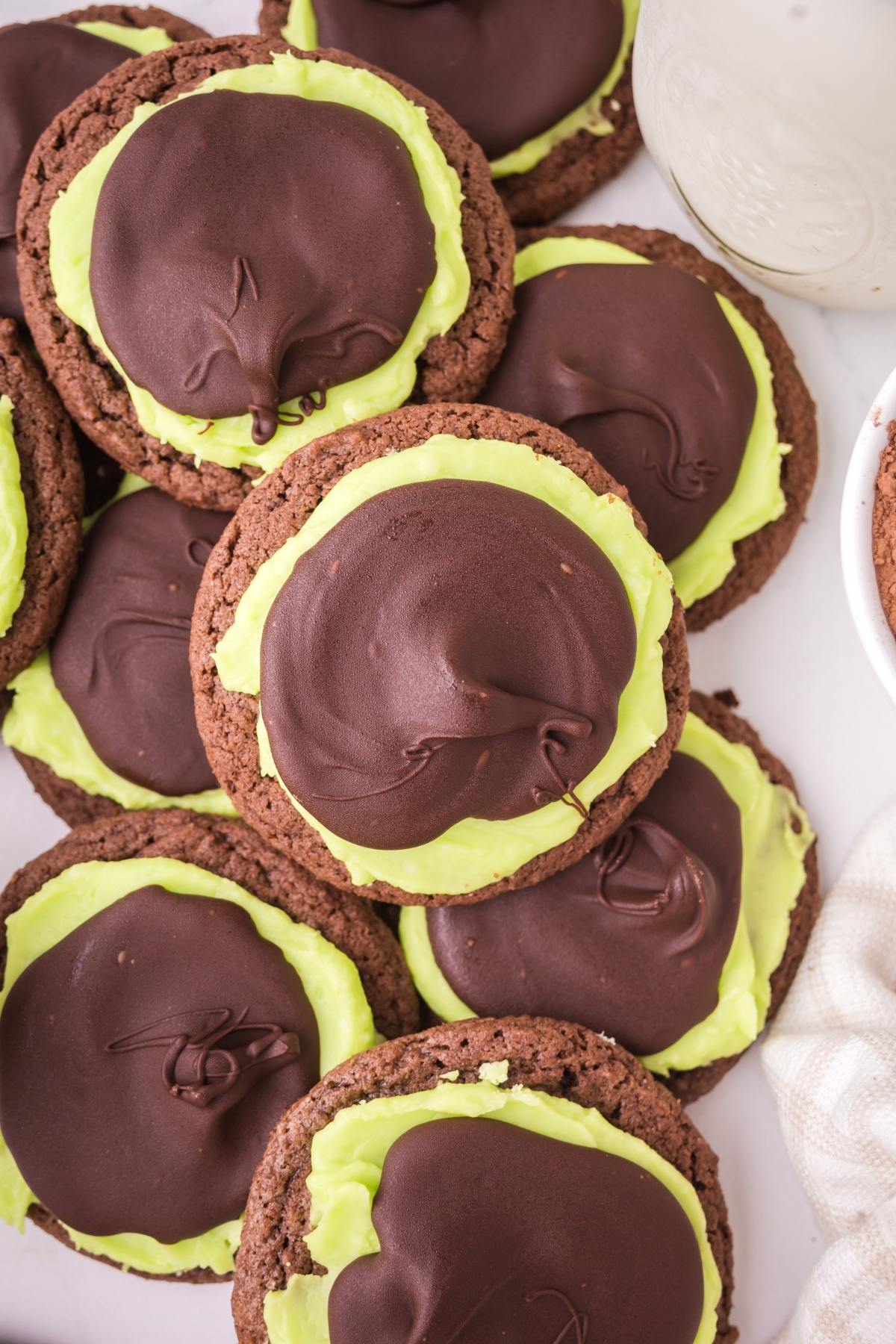 Chocolate cookies topped with green frosting and a layer of chocolate, stacked closely together.