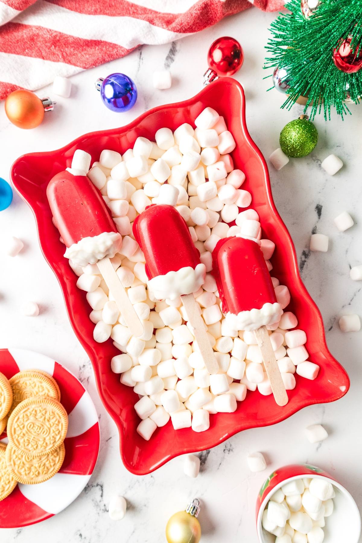 Three red popsicles with white tips on sticks, arranged on mini marshmallows in a festive red tray.