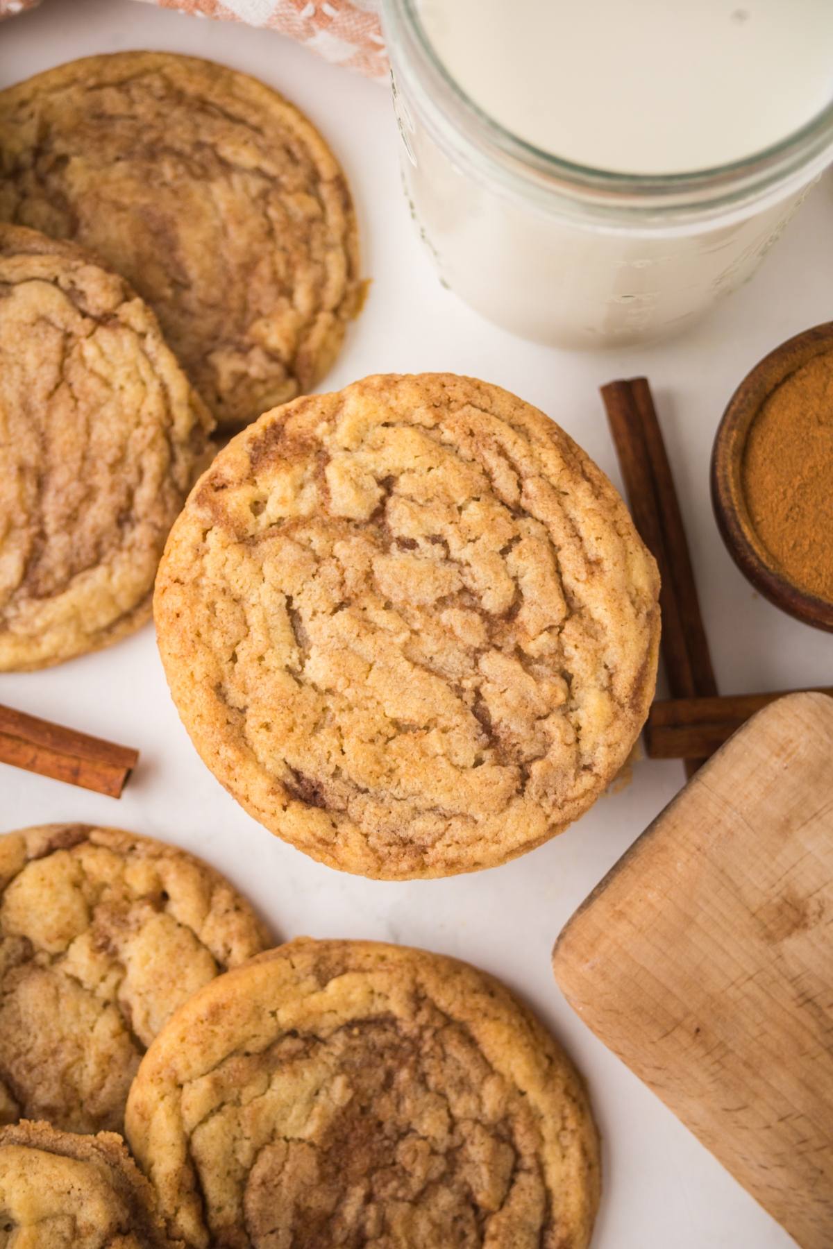 A close-up of cinamon sugar cookies with a glass of milk, cinnamon sticks, and ground cinnamon nearby.