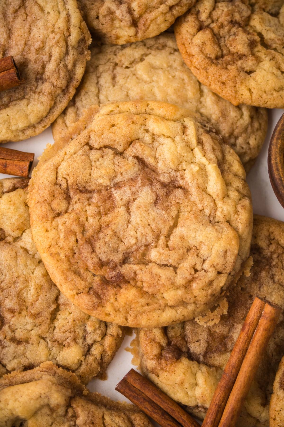 A close-up of cinnamon roll cookies with cinnamon sticks scattered around them.