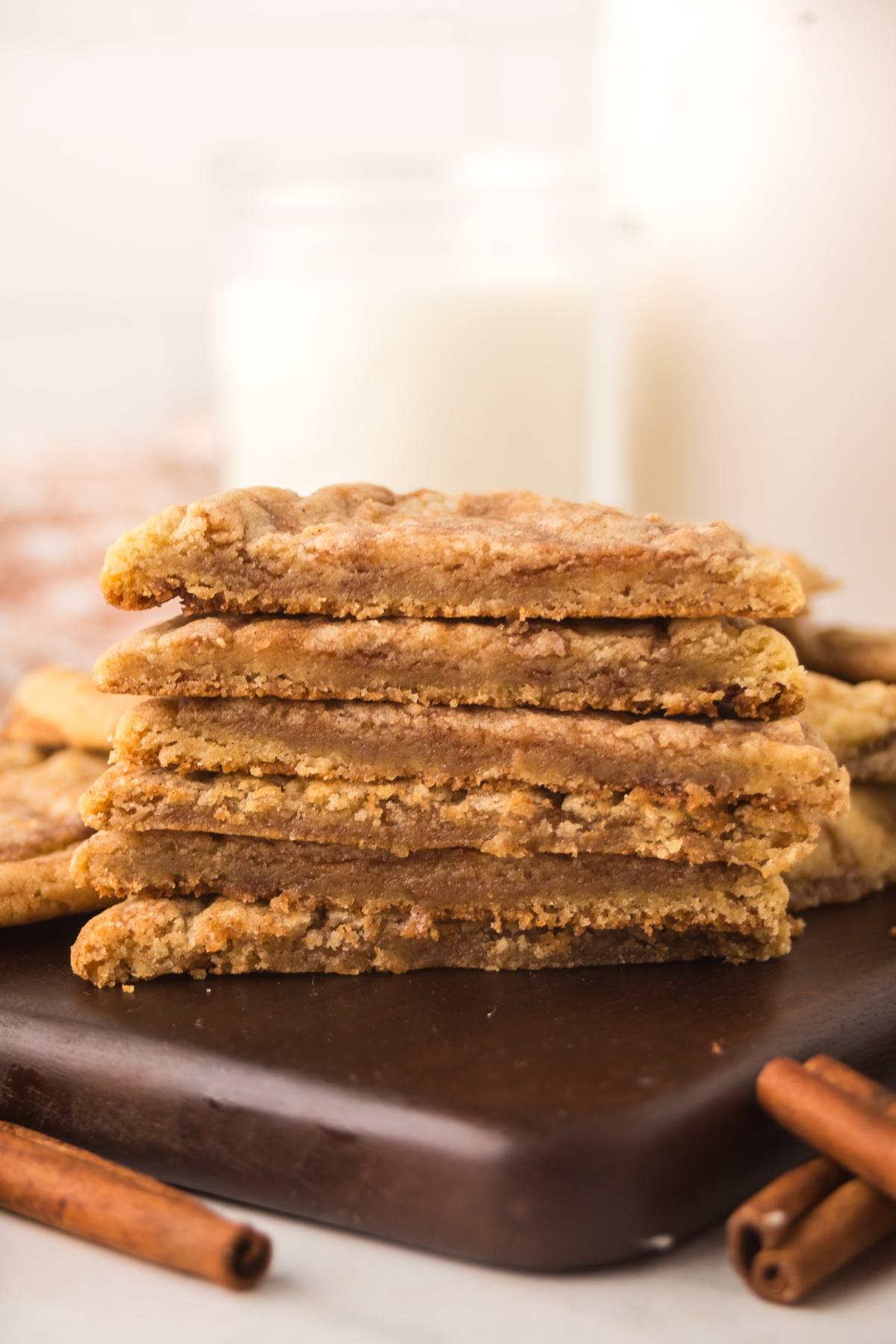 Stack of six chewy cookies on a dark board with cinnamon sticks and a glass of milk in the background.