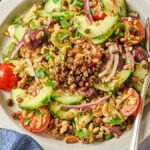 A plate of crispy lentil salad with fresh cucumbers, cherry tomatoes, onions, olives, and wholesome grains.