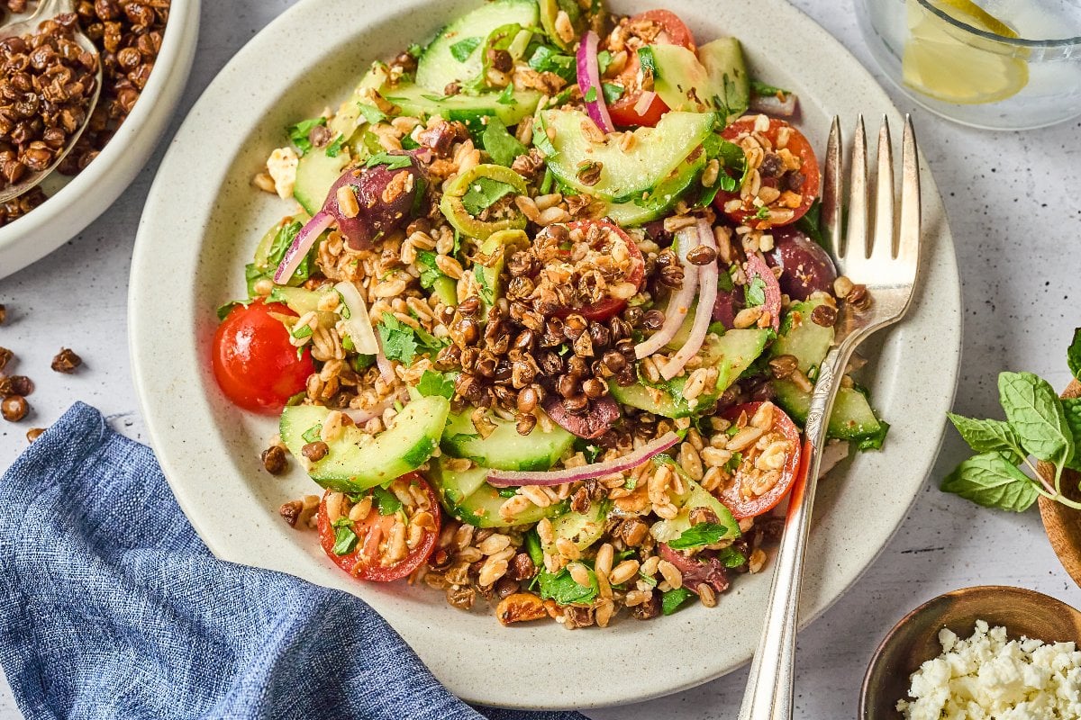 A plate of crispy lentil salad with tomatoes, cucumbers, onions, olives, fresh herbs, and crunchy lentils, served with a fork.