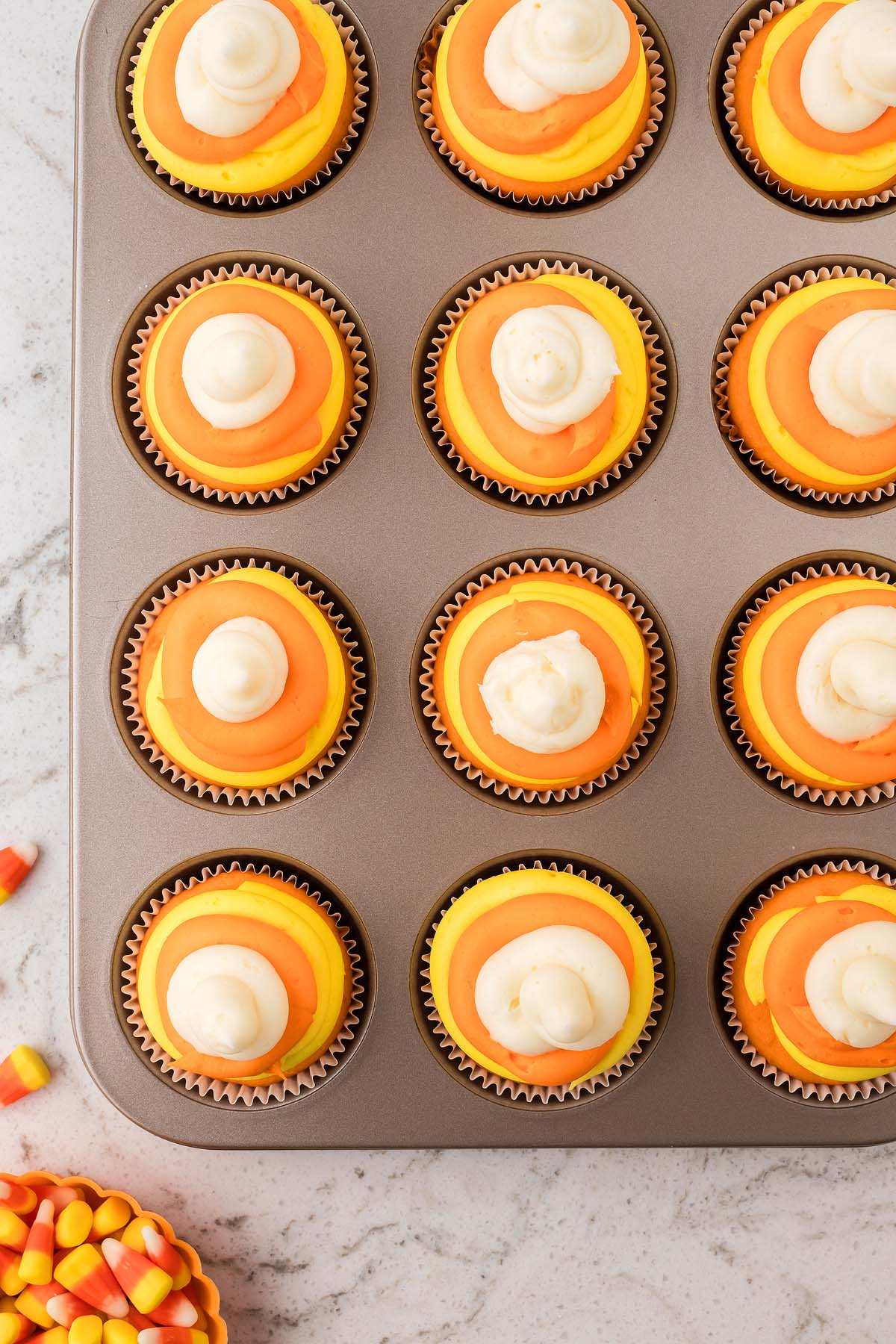 Candy corn cupcakes in a muffin tin with orange, yellow, and white frosting, perfectly resembling the classic Halloween treat.