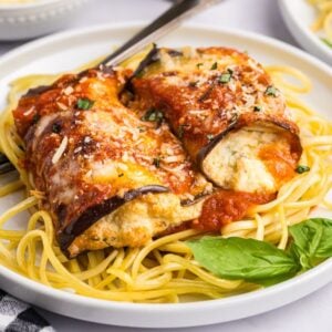 Eggplant rollatini - rolled eggplant stuffed with ricotta on spaghetti, topped with marinara sauce and grated cheese, garnished with basil.