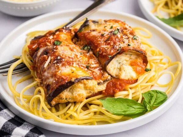 Eggplant rollatini - rolled eggplant stuffed with ricotta on spaghetti, topped with marinara sauce and grated cheese, garnished with basil.
