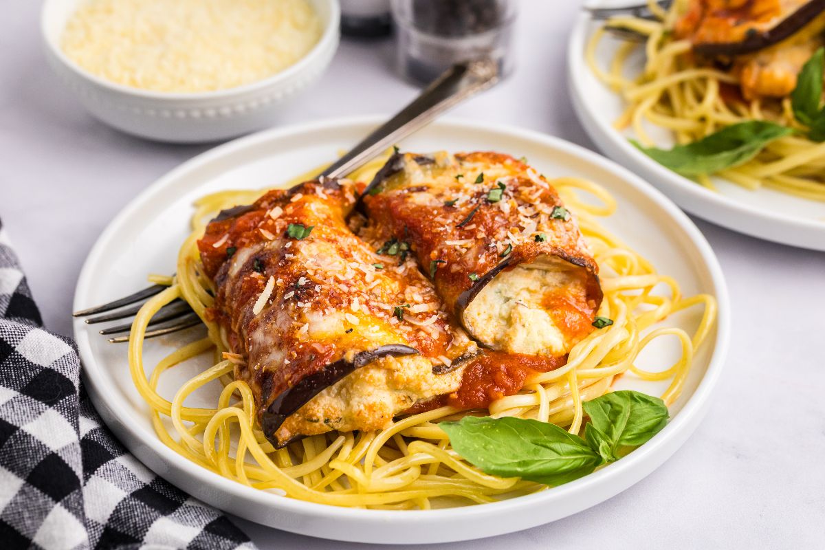 Eggplant rollatini with tomato sauce served over spaghetti, garnished with fresh basil, creates a vibrant and delicious plate.