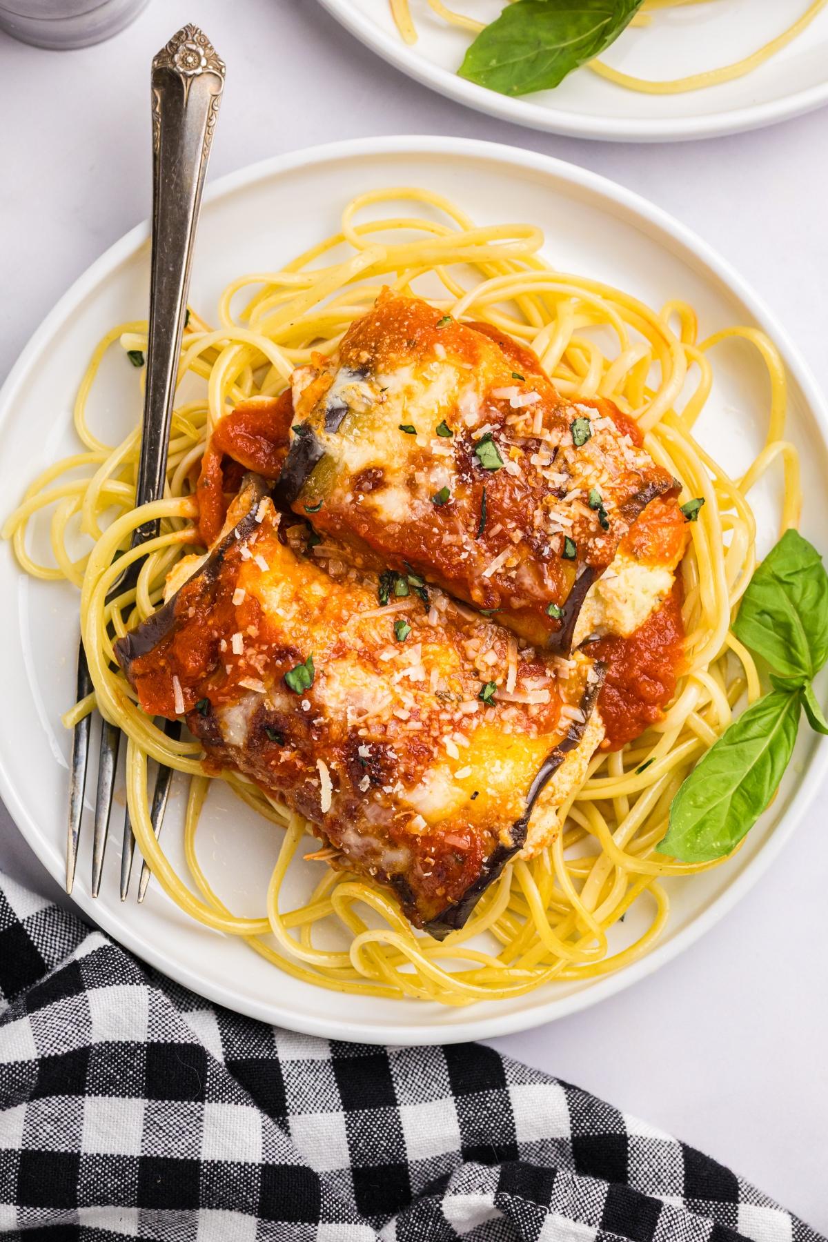 Plate of spaghetti topped with cheesy baked eggplant rollatini and tomato sauce, garnished with basil.