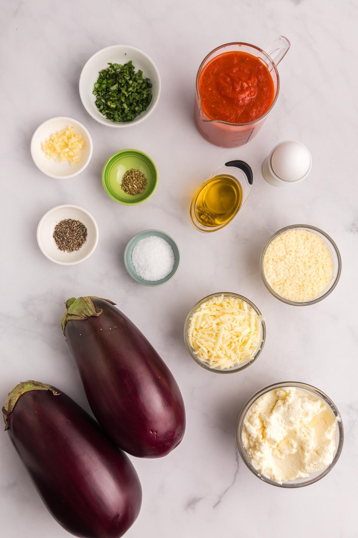 Eggplants, cheese, tomato sauce, egg, oil, salt, pepper, herbs, and garlic on a marble surface.