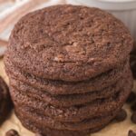 A stack of espresso brownie cookies surrounded by chocolate chips on parchment paper.