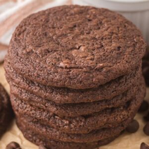 A stack of espresso brownie cookies surrounded by chocolate chips on parchment paper.