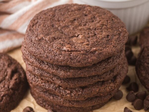 A stack of espresso brownie cookies surrounded by chocolate chips on parchment paper.