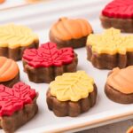 A tray of fall cake bites shaped like pumpkins and leaves, decorated with red and yellow icing.