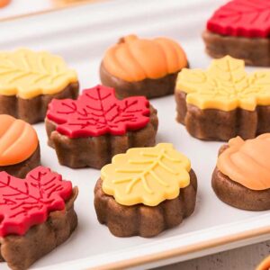 A tray of fall cake bites shaped like pumpkins and leaves, decorated with red and yellow icing.