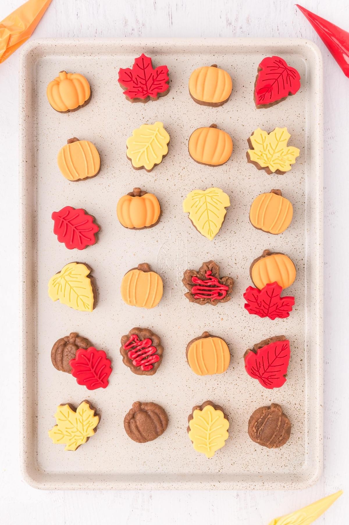 Cake pop bites shaped like pumpkins and autumn leaves arranged neatly on a baking sheet.