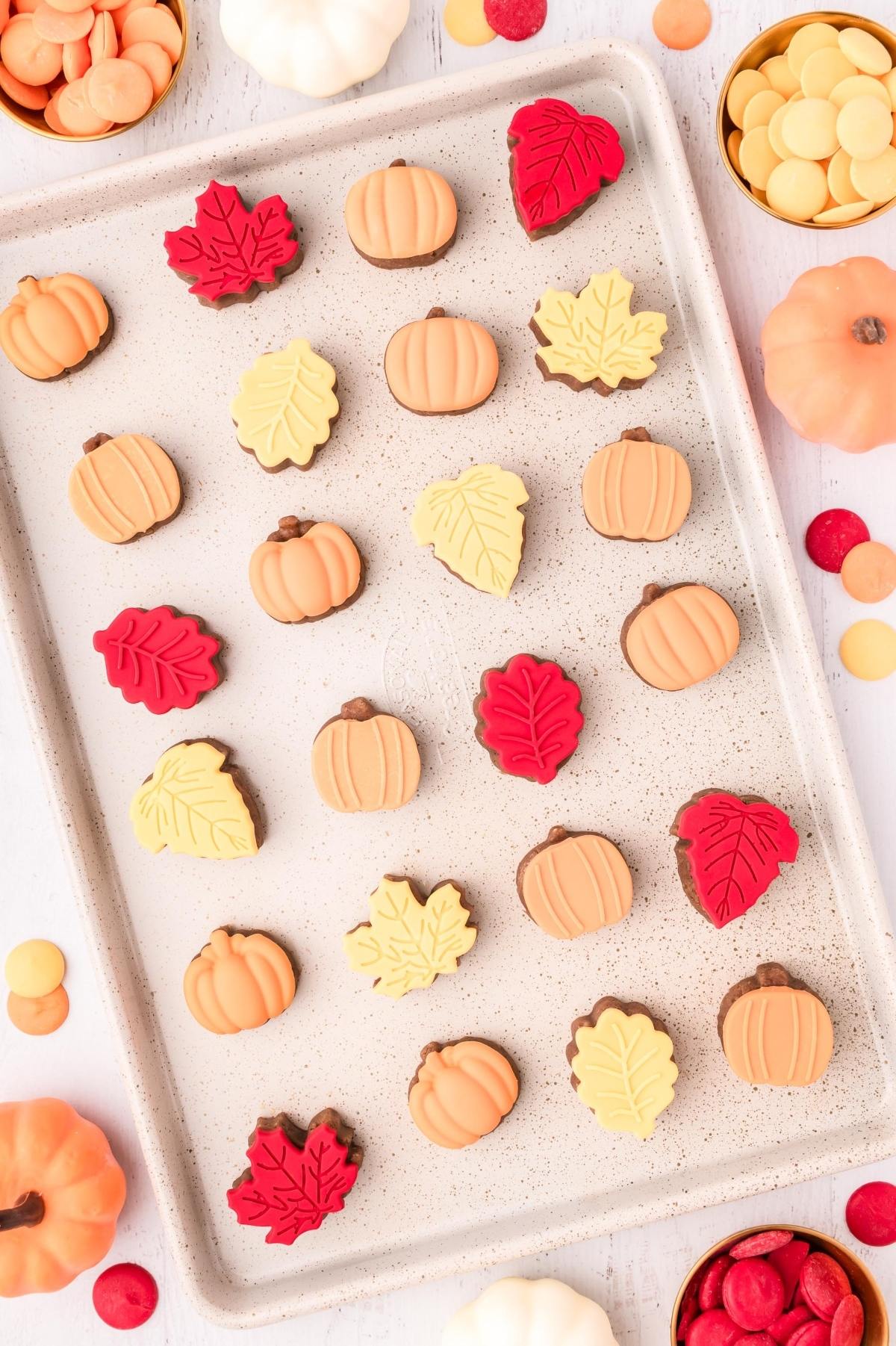 A baking sheet with leaf and pumpkin-shaped fall cake bites in red, yellow, and orange, surrounded by candies.