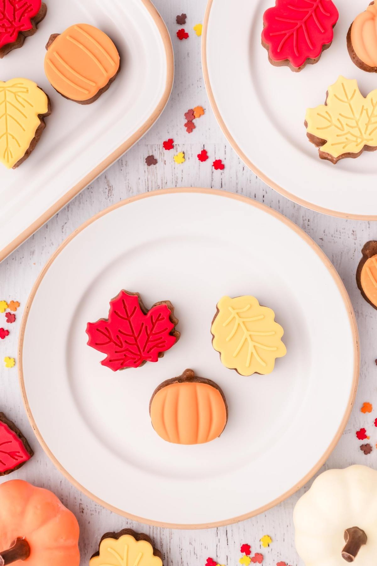 Autumn-themed cake pop bites shaped like pumpkins and leaves on white plates, surrounded by colorful confetti.