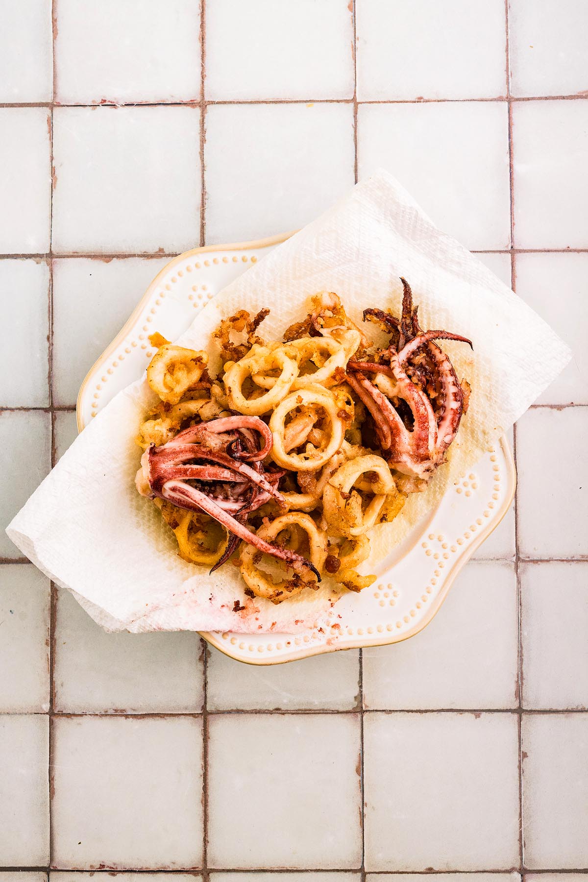 Crispy fried fritto misto, served on a paper towel-lined plate atop a tiled surface.