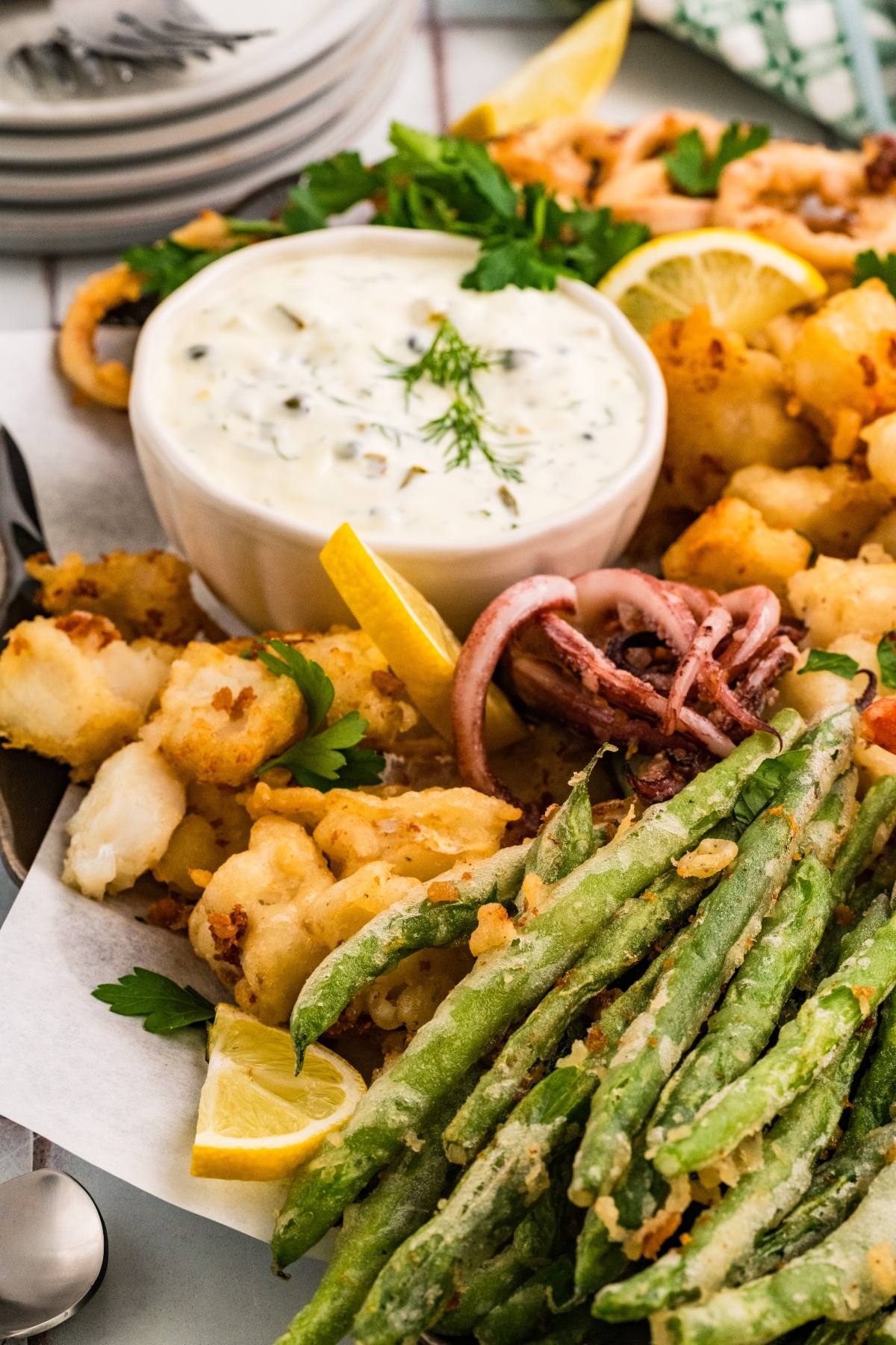 A platter with fried green beans, calamari, lemon wedges, and a bowl of creamy dipping sauce.