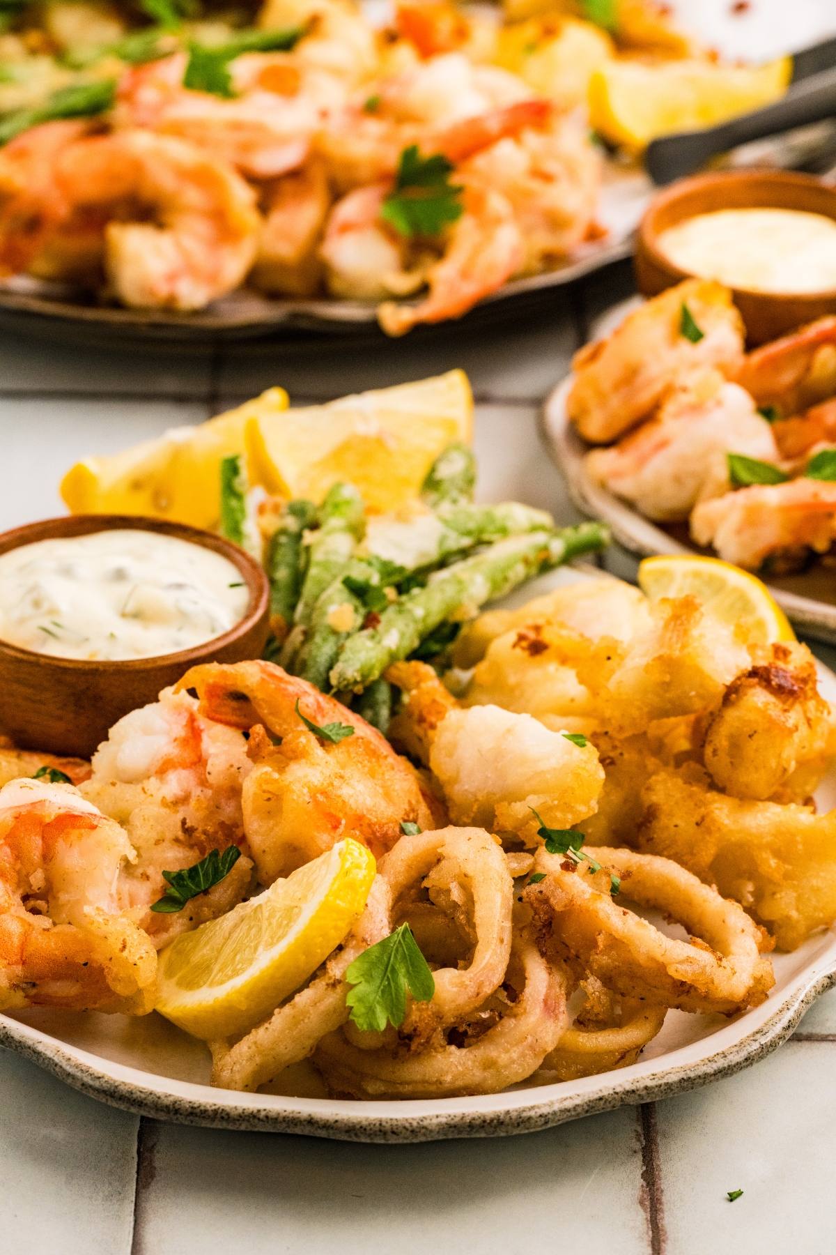 A plate of fried seafood with lemon wedges, green beans, and dipping sauce, garnished with fresh parsley.