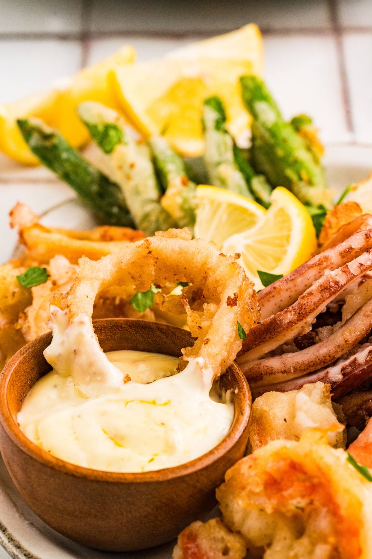 A plate of fried calamari with lemon wedges, dipping sauce, and green vegetables in the background.