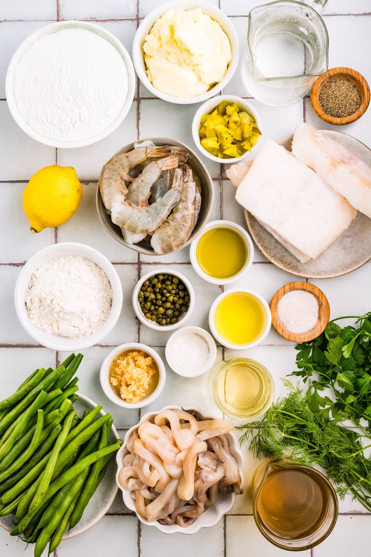 Assorted ingredients for a seafood dish, including shrimp, fish, squid, lemons, green beans, and seasonings.