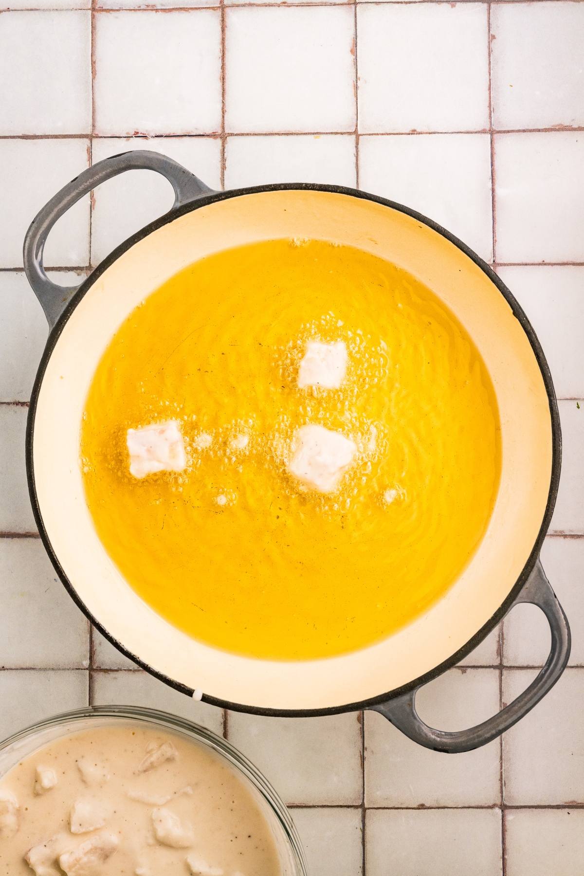 A pot of hot oil with three pieces of breaded food frying; more pieces in a bowl nearby.