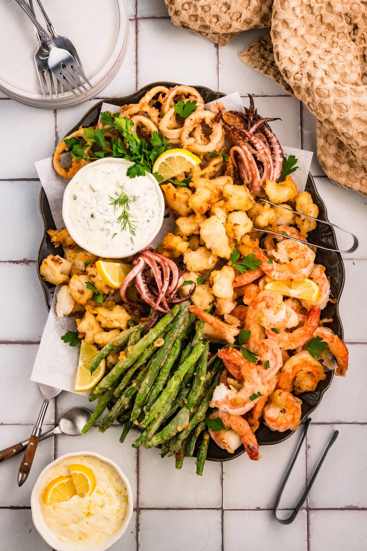 Seafood platter with shrimp, fried calamari, green beans, lemon wedges, and dipping sauces on a serving tray.