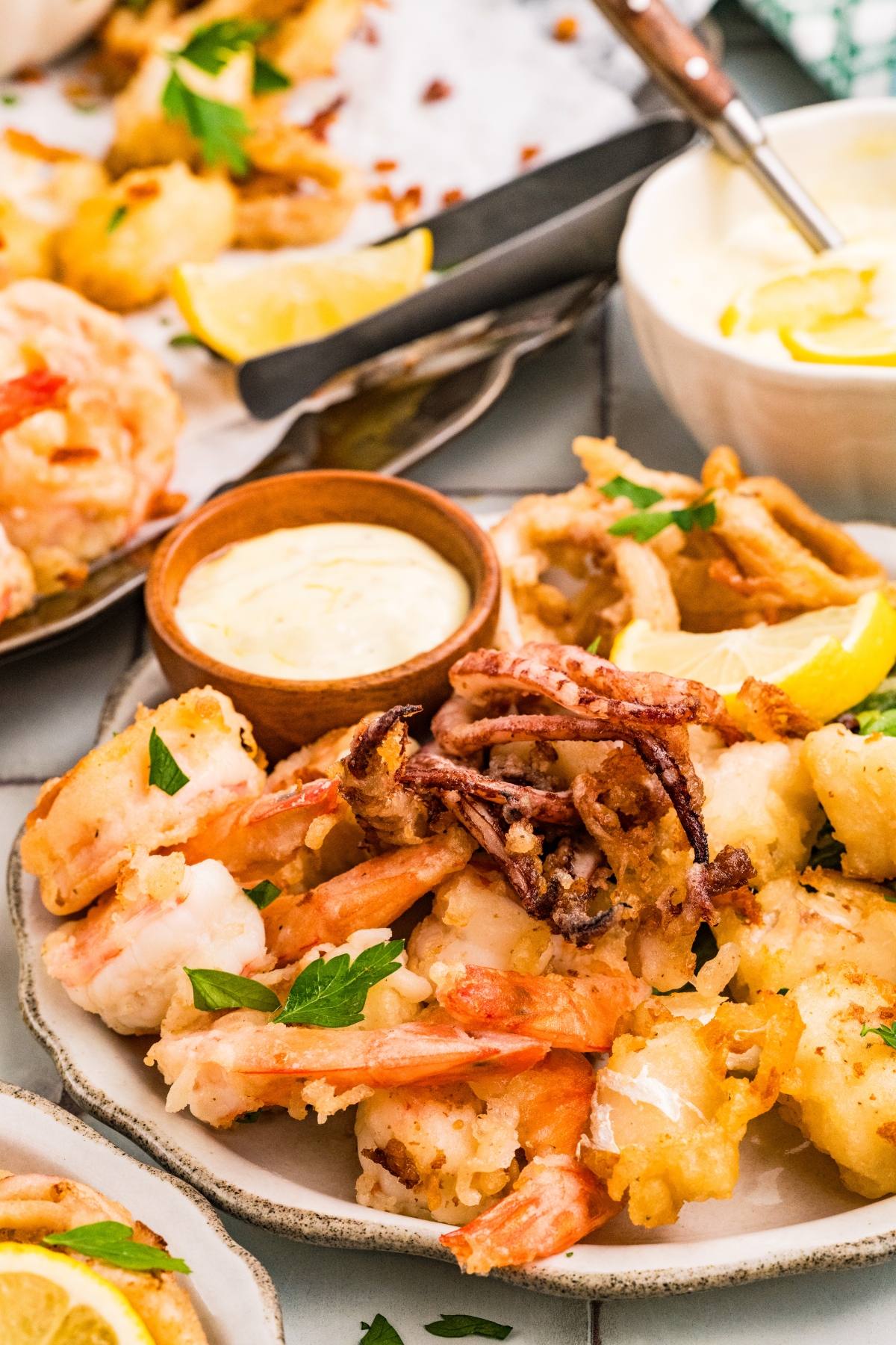 A plate of fried seafood with shrimp, calamari, dipping sauce, and lemon wedges, garnished with parsley.