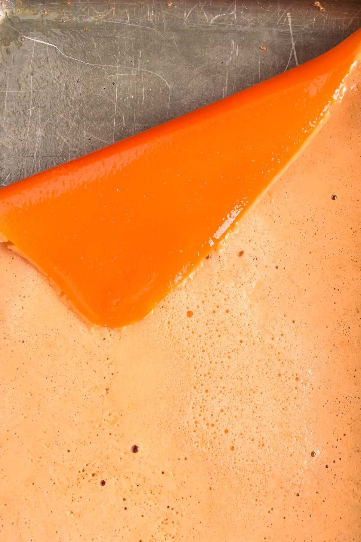 A close-up of an orange jello sheet being peeled from a flat metal surface.