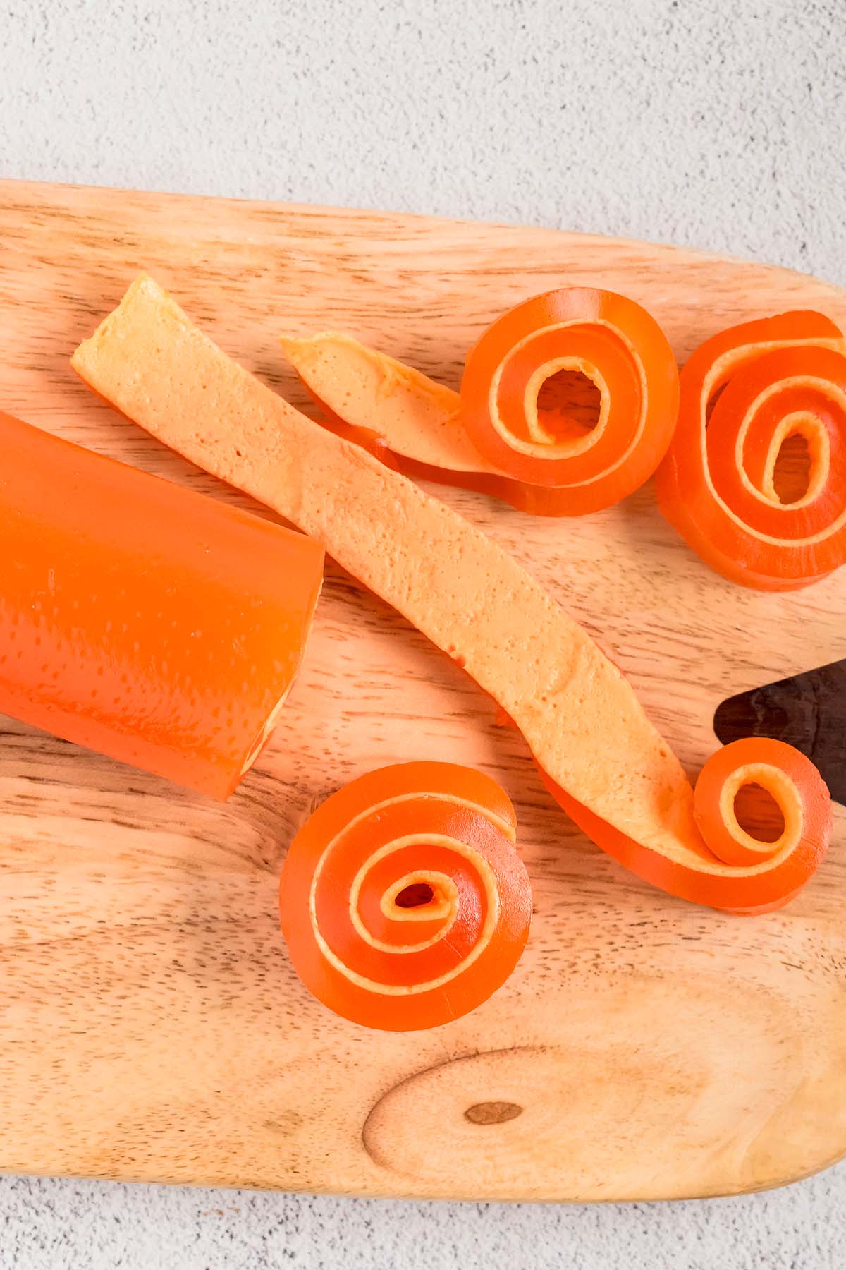 Orange jello strips and rolls on a wooden board.