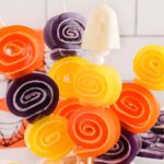 Colorful orange, yellow, and purple Halloween Jello Roll Ups on skewers, arranged in a festive display.