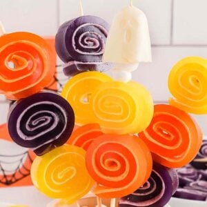 Colorful orange, yellow, and purple Halloween Jello Roll Ups on skewers, arranged in a festive display.
