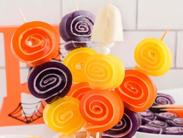 Colorful orange, yellow, and purple Halloween Jello Roll Ups on skewers, arranged in a festive display.