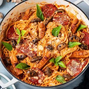 Halloween Pasta featuring spaghetti with tomato sauce, mushrooms, basil, and finger-shaped sausages in a white pot on the table.